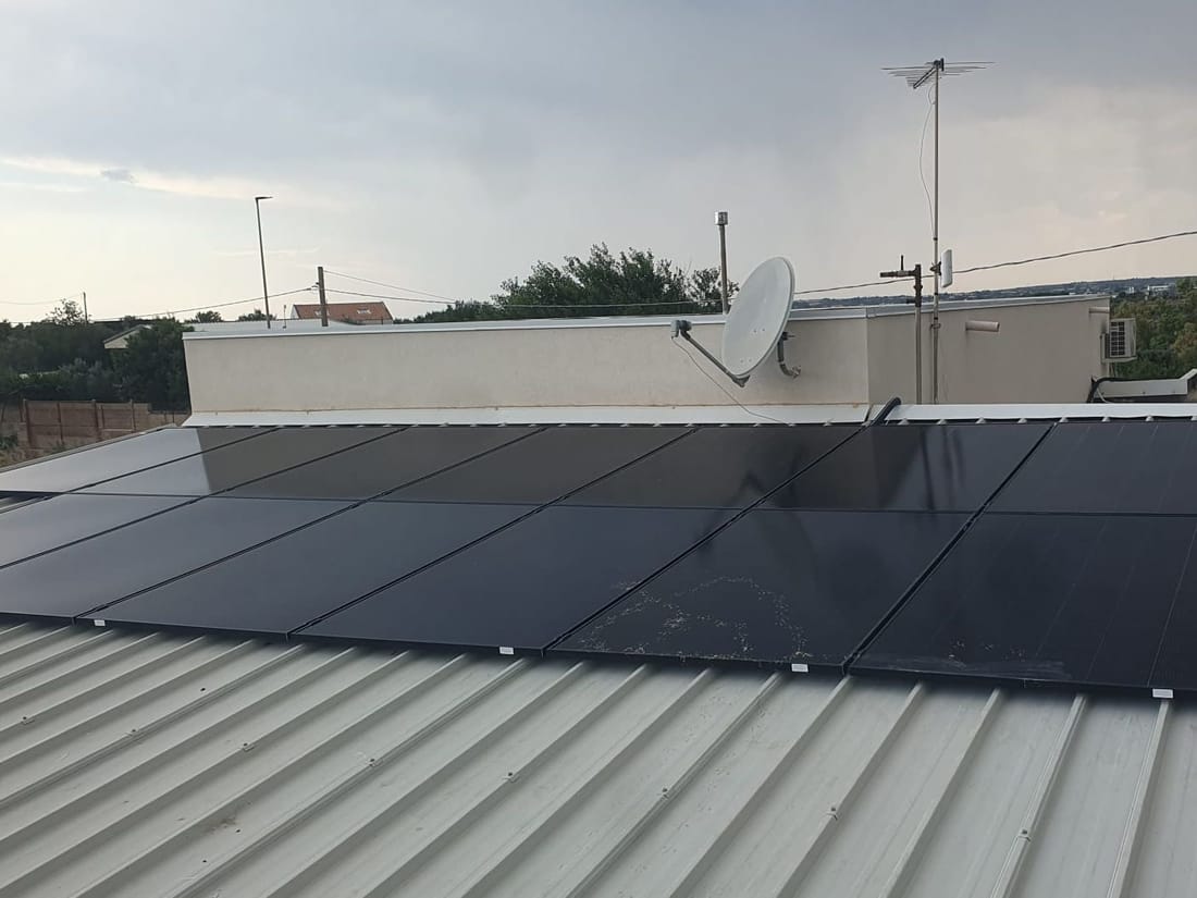 Pannelli fotovoltaici neri su un tetto in lamiera di una casa, con la parabola sul parapetto e il cielo nuvoloso