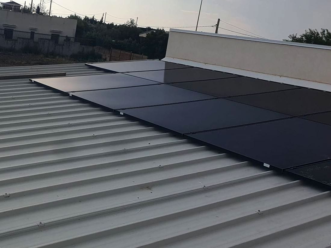 Pannelli fotovoltaici neri su un tetto in lamiera, accanto al parapetto, con il sole basso